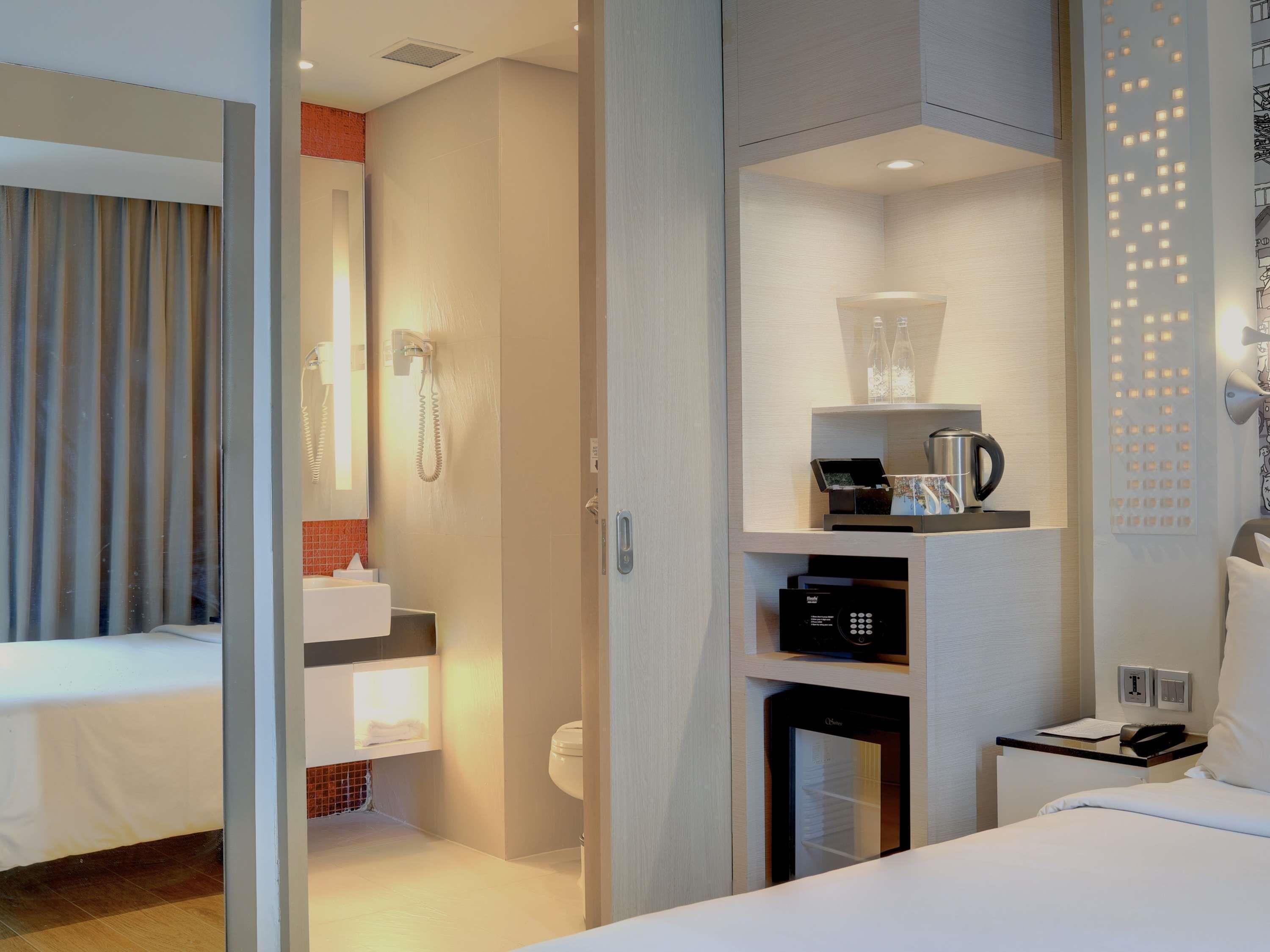 A hotel room with a bed, a bathroom with a shower, a coffee machine, and a minibar.