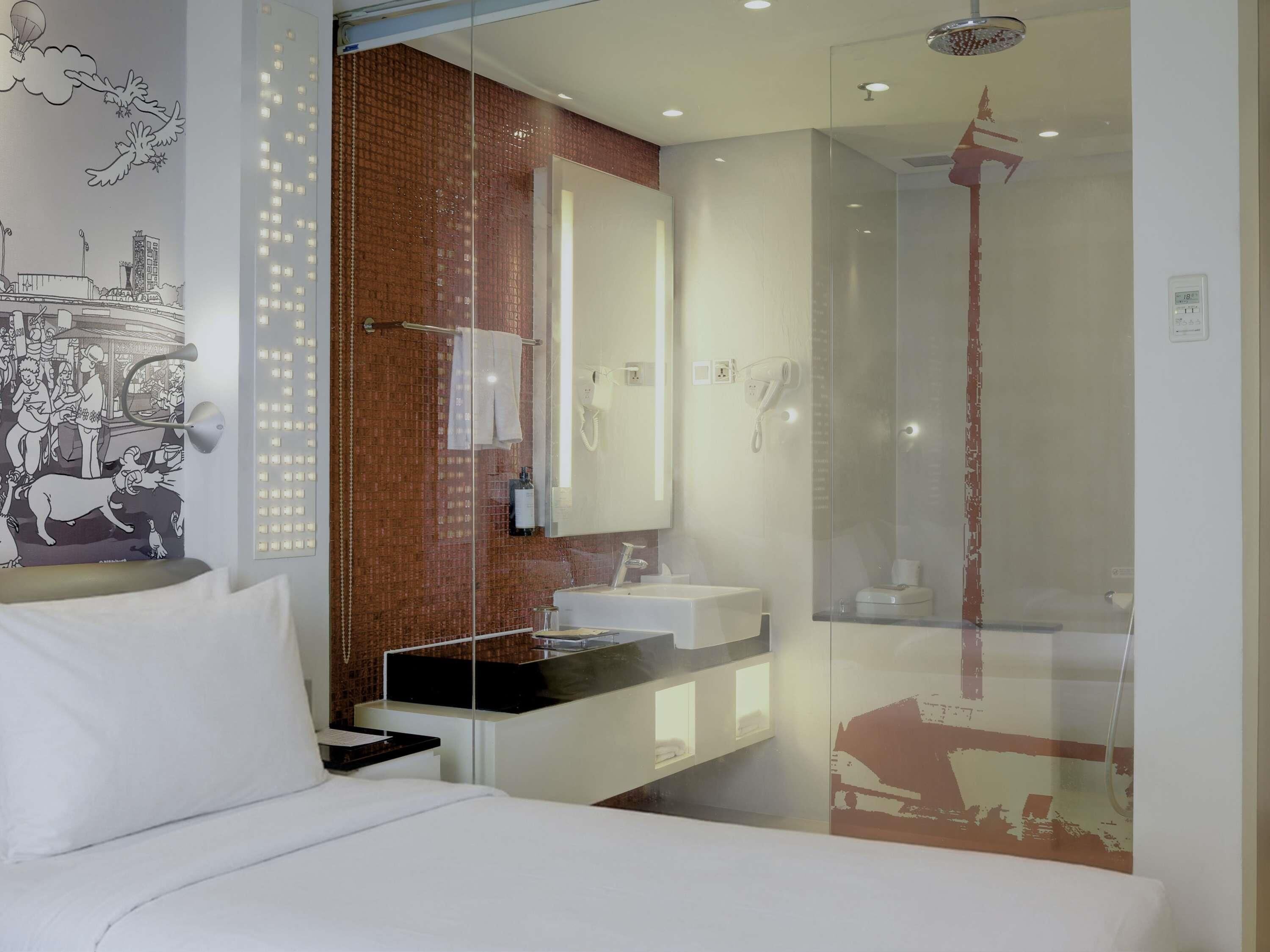 Een moderne hotelkamer met een bed, een badkamer met douche en een grote spiegel.