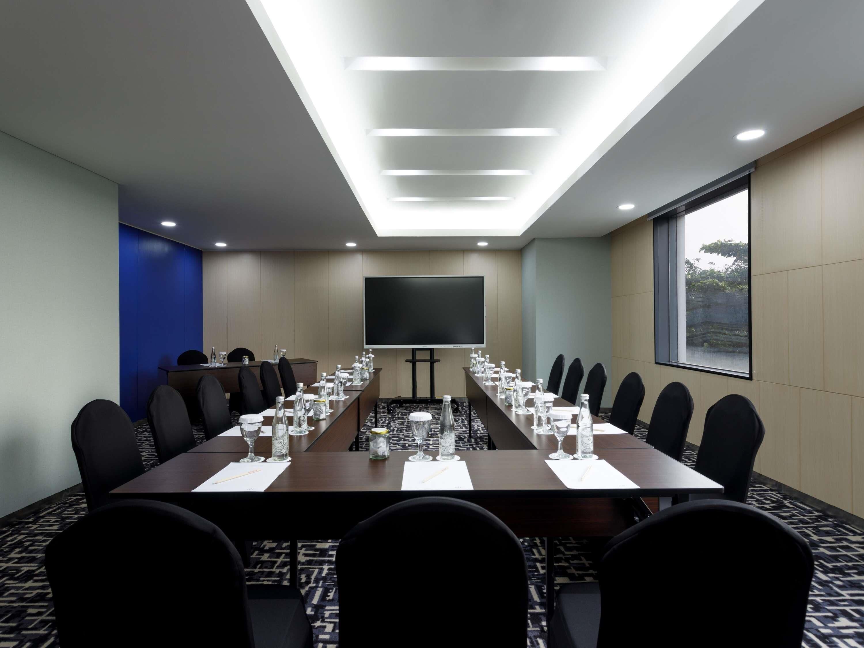 A conference room with a long table, chairs, a screen, and a window.