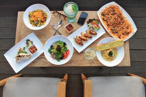 Puisella pöydällä on erilaisia ruokia, kuten pastaa, salaatteja ja pizzaa, sekä ruokailuvälineet ja lasi vettä.