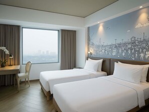 A hotel room with two beds, a desk with a lamp, a chair, and a large window with curtains. - Mercure Jakarta Simatupang (Jakarta)