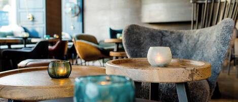 Un rincón acogedor con mesas redondas de madera, sillas con cojines y un sofá suave de color gris.