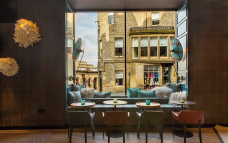 A cozy interior with a view of a historic building, featuring a seating area with tables and chairs, and a large window.
