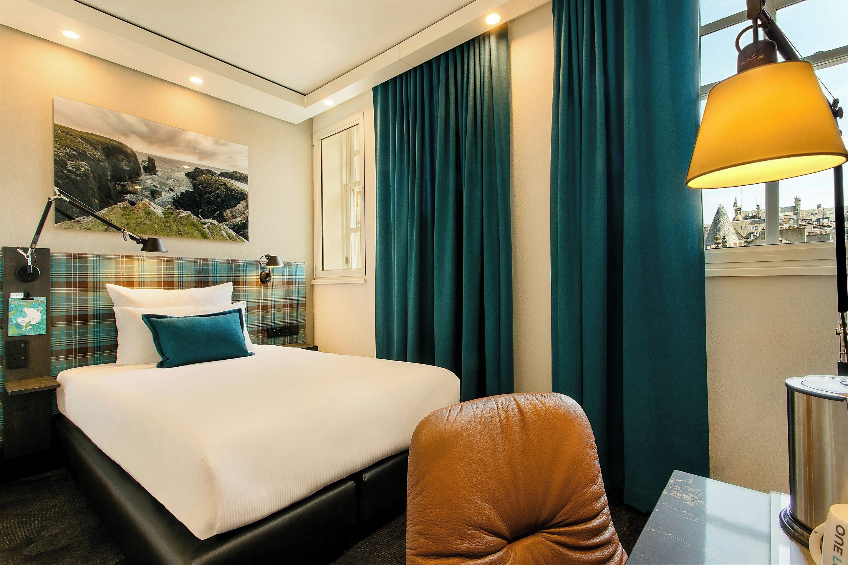 A hotel room with a bed, a desk, a chair, a lamp, and a window with curtains.