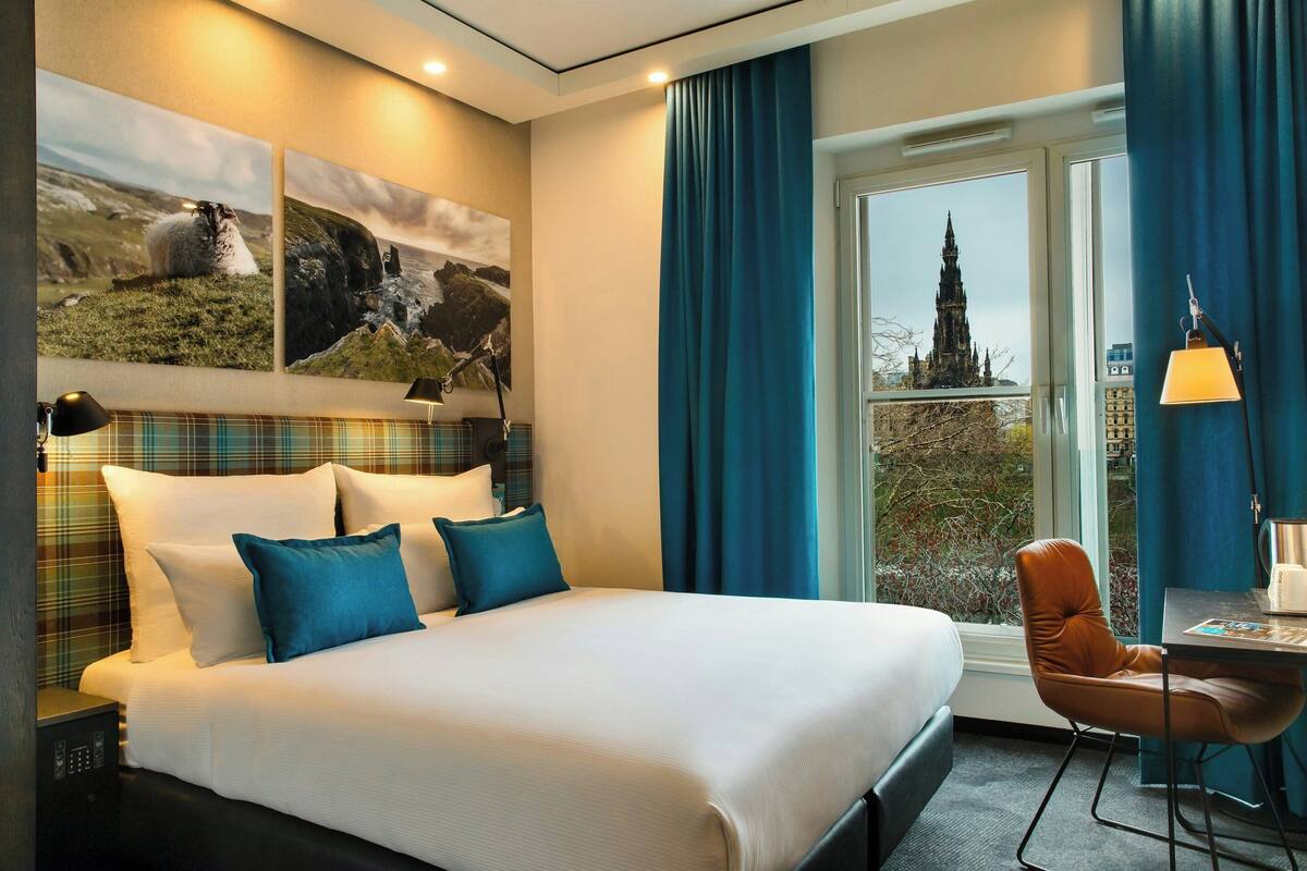 Une chambre d’hôtel avec un grand lit, un bureau avec une chaise et une fenêtre donnant sur un immeuble.