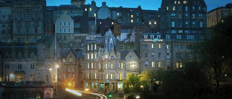 A historic building with a prominent tower, a sign for 'Motel One', and a well-lit street with traffic lights.