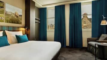 Une chambre d’hôtel avec un grand lit, un canapé, une petite table et une vue sur un immeuble par la fenêtre.