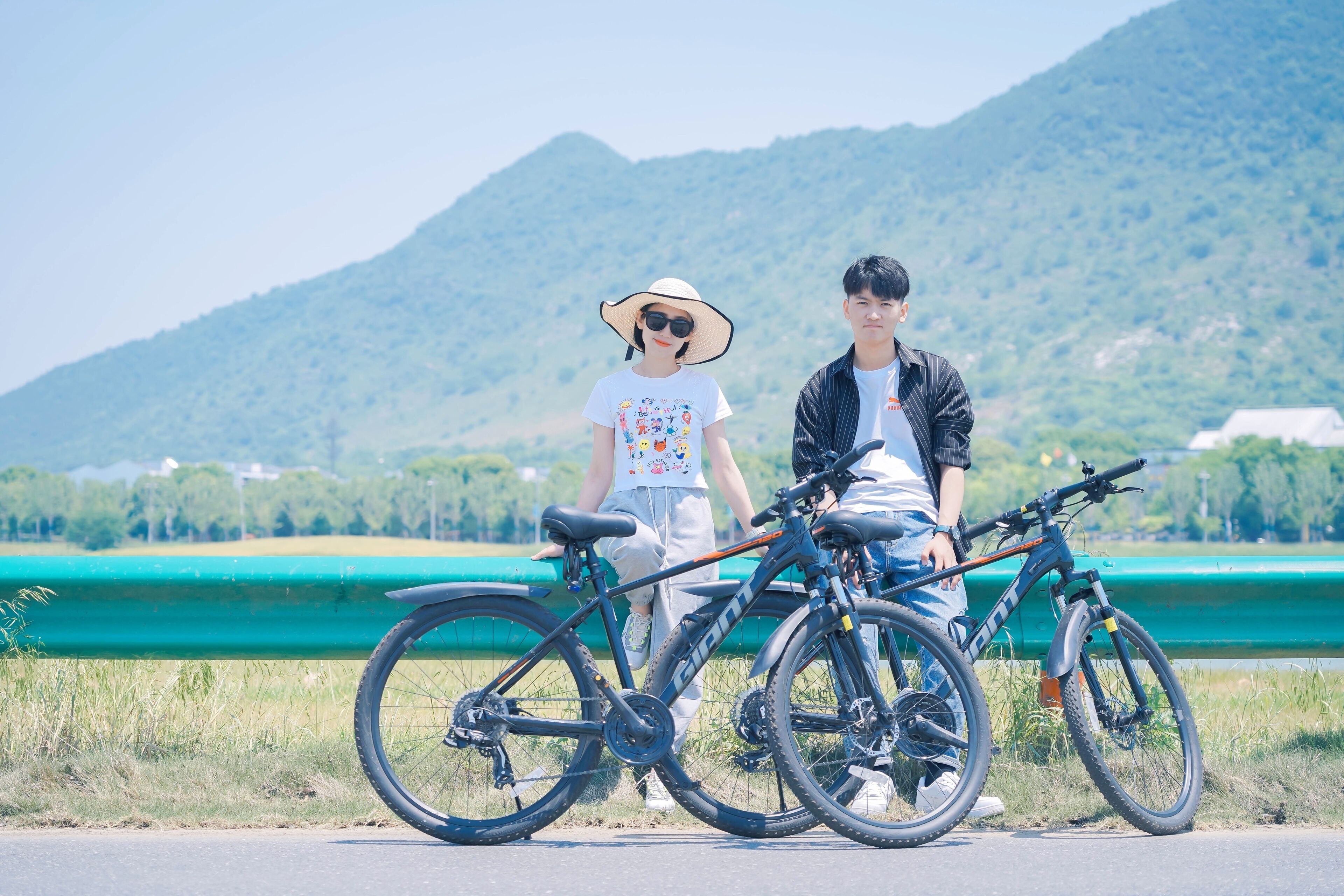 Duas bicicletas estacionadas em uma estrada, com uma barreira verde e montanhas ao fundo.