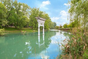 A serene park with a traditional pavilion by a calm river, surrounded by lush greenery.