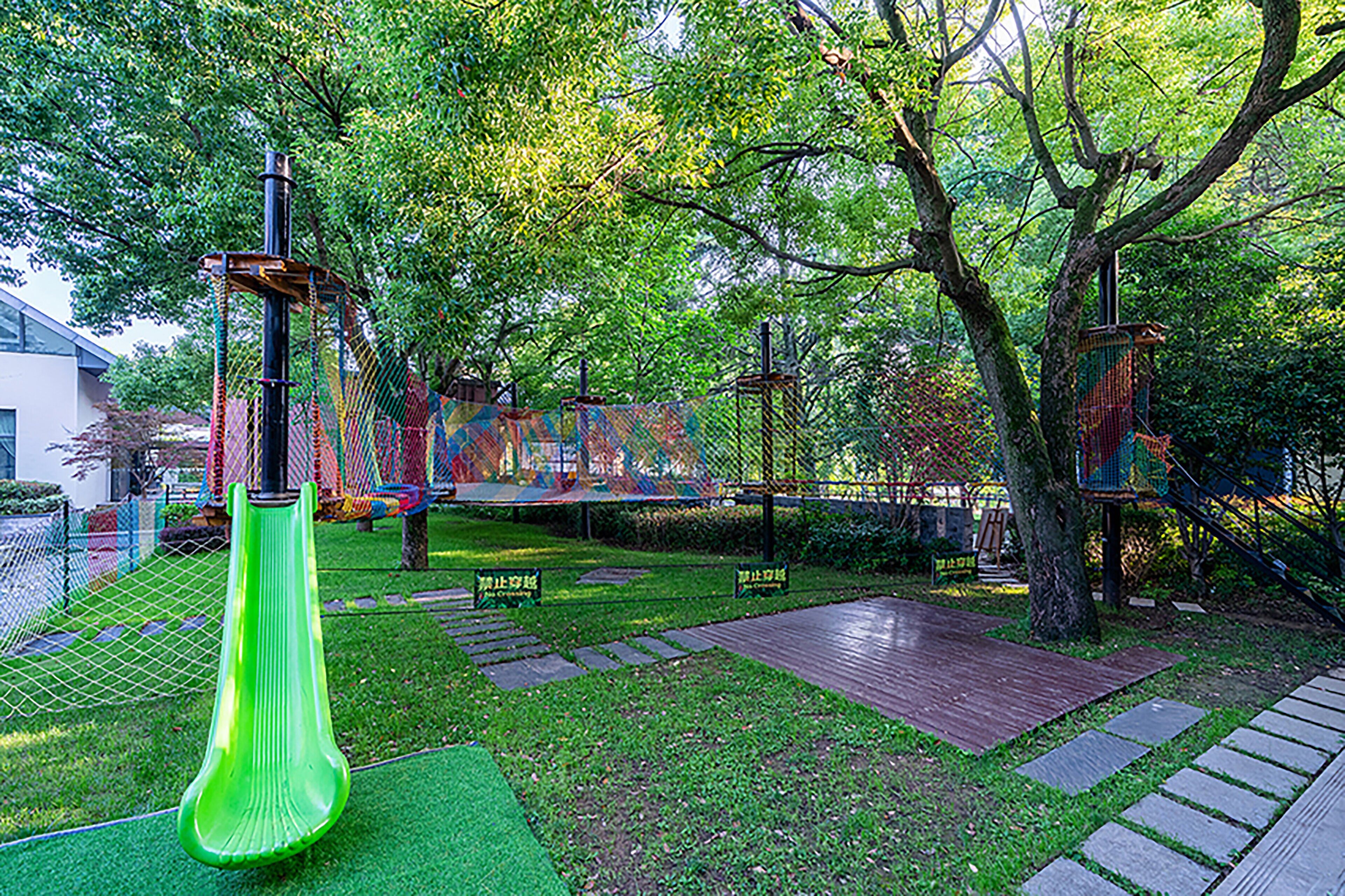 Un'area giochi con uno scivolo verde, strutture per arrampicarsi e un recinto alberato.