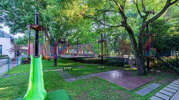 Un'area giochi con uno scivolo verde, strutture per arrampicarsi e un recinto alberato.