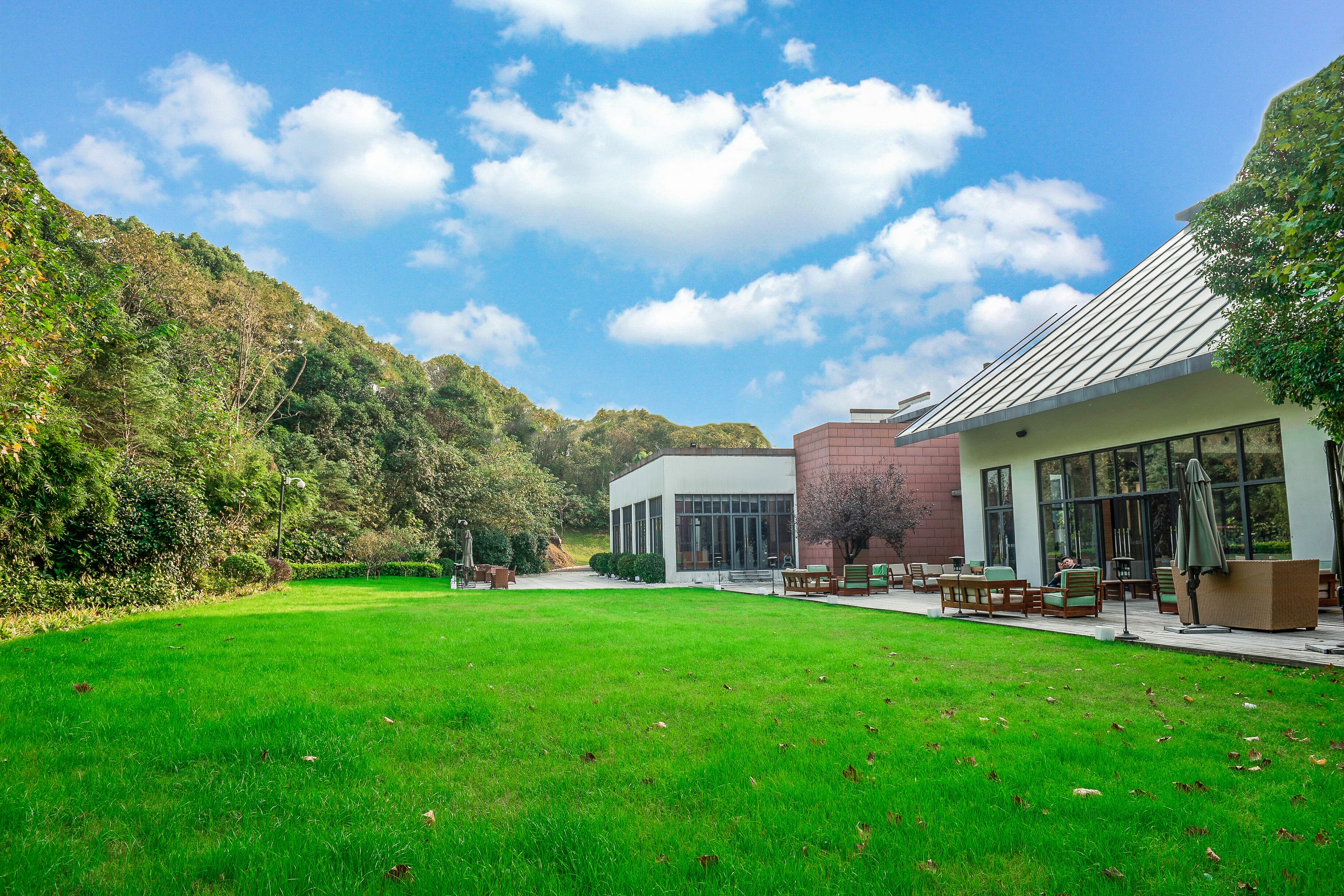 A modern building with a glass facade, a well-maintained lawn, and a view of a forested hillside.