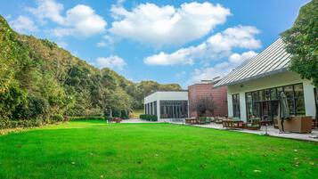 A modern building with a glass facade, a well-maintained lawn, and a view of a forested hillside.