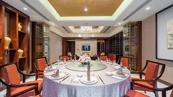A conference room with a round table set for a meeting, surrounded by chairs, with a chandelier above and a large painting on the wall.