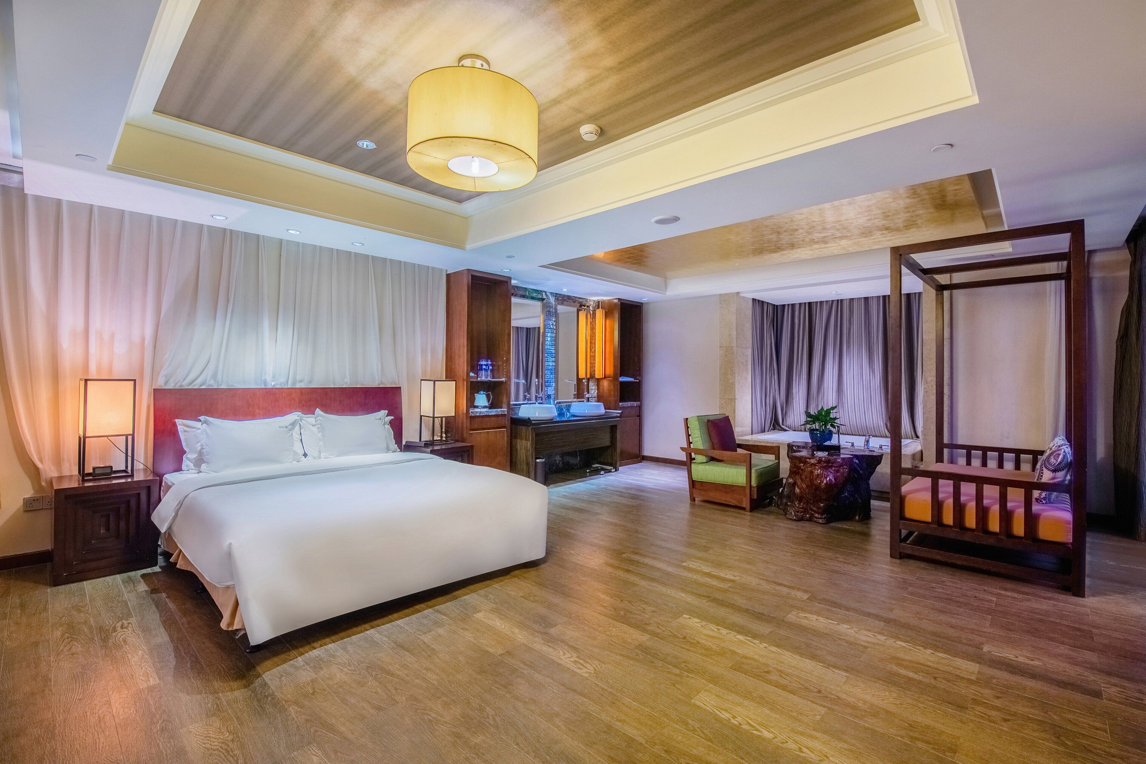 Habitación de hotel con una cama grande, un escritorio con una computadora, una silla, una mesita con una planta y un balcón con barandilla.