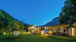 A well-lit outdoor area with a grassy lawn, seating arrangements, and a building with large windows. - Holiday Inn Resort Chaohu Hot Spring by IHG (Hefei)
