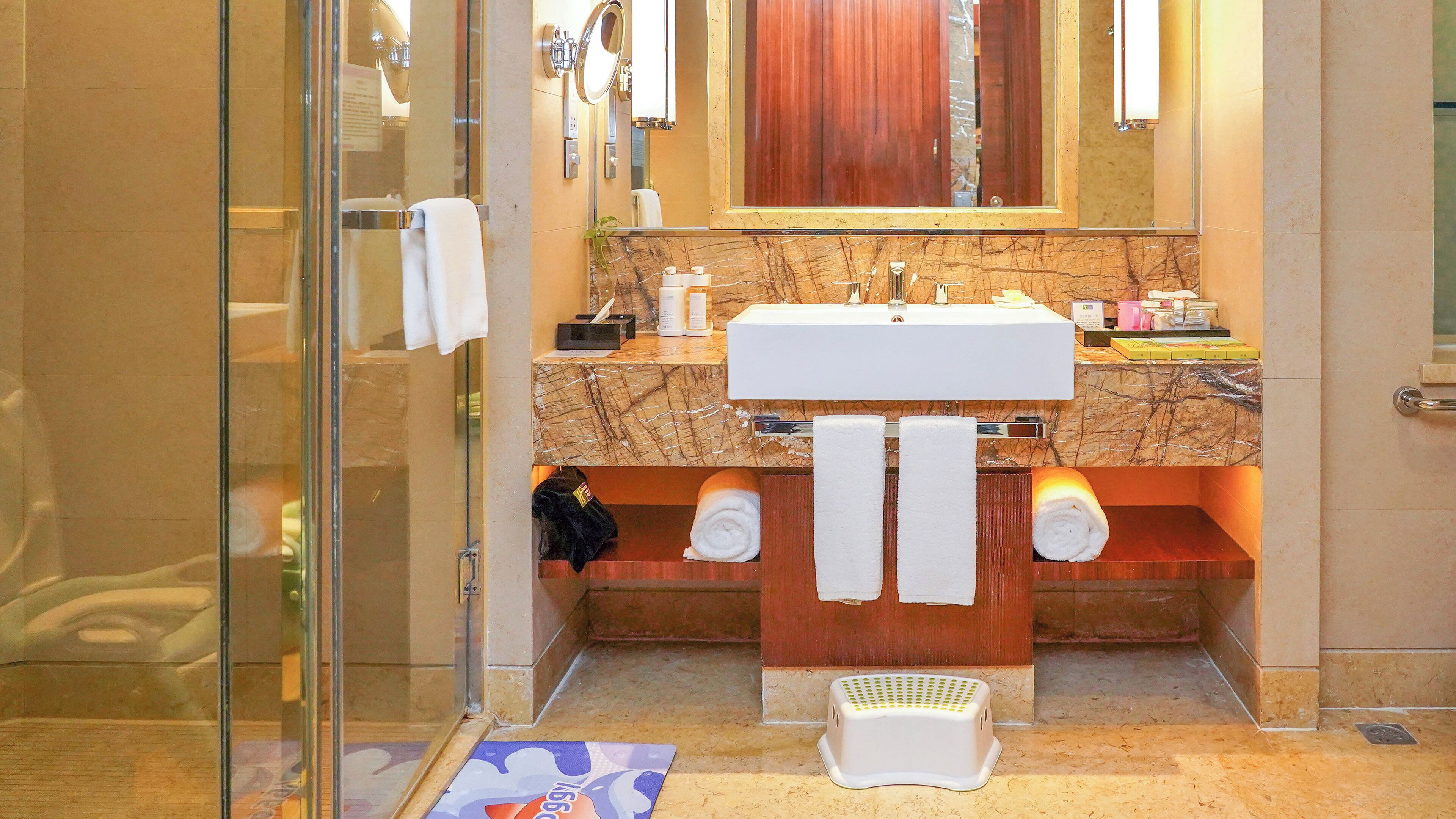 A bathroom with a glass shower enclosure, a white sink, and a wooden vanity.