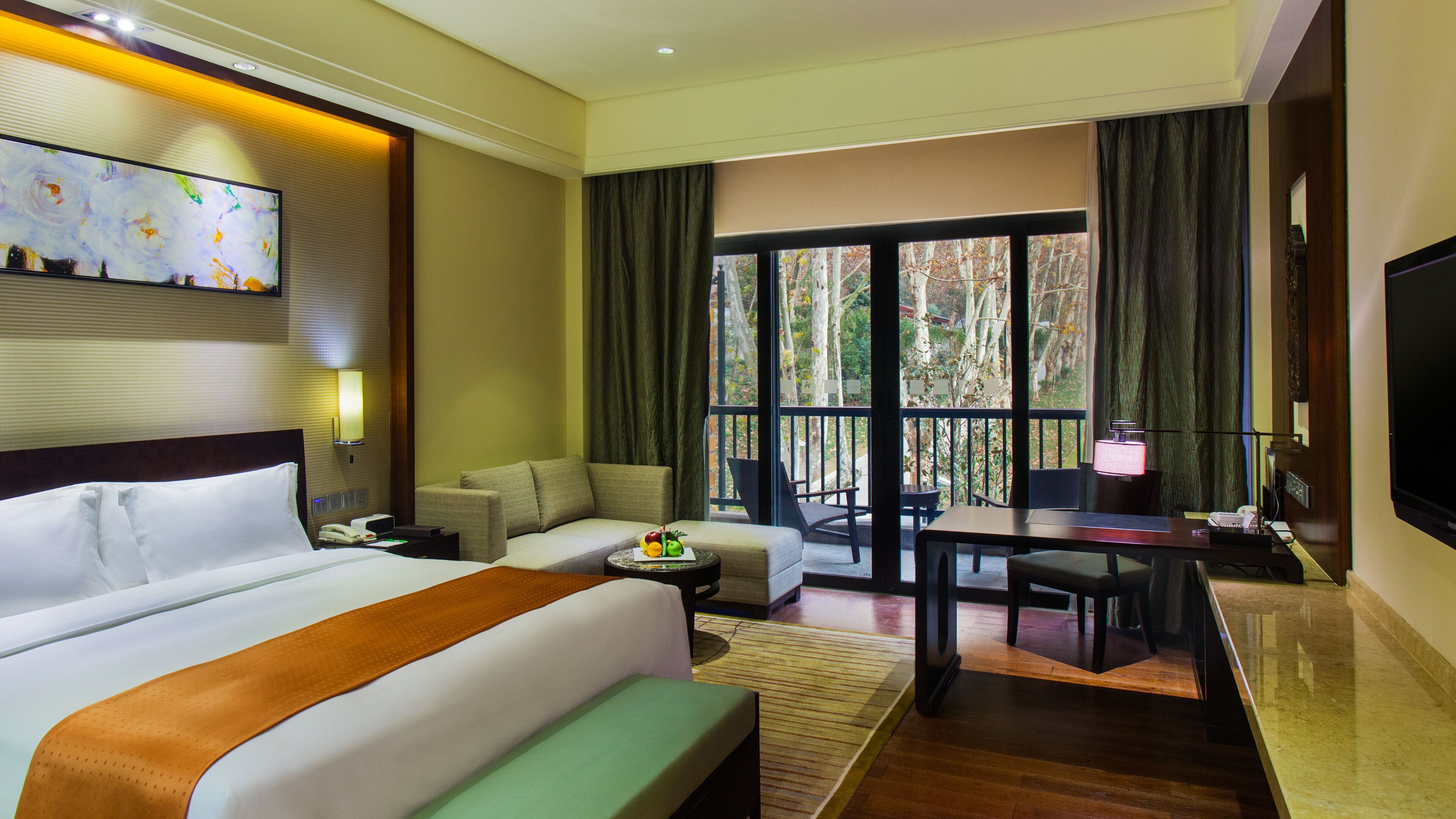 Une chambre d’hôtel avec un grand lit, un bureau, une chaise, une télévision et un balcon donnant sur la verdure.