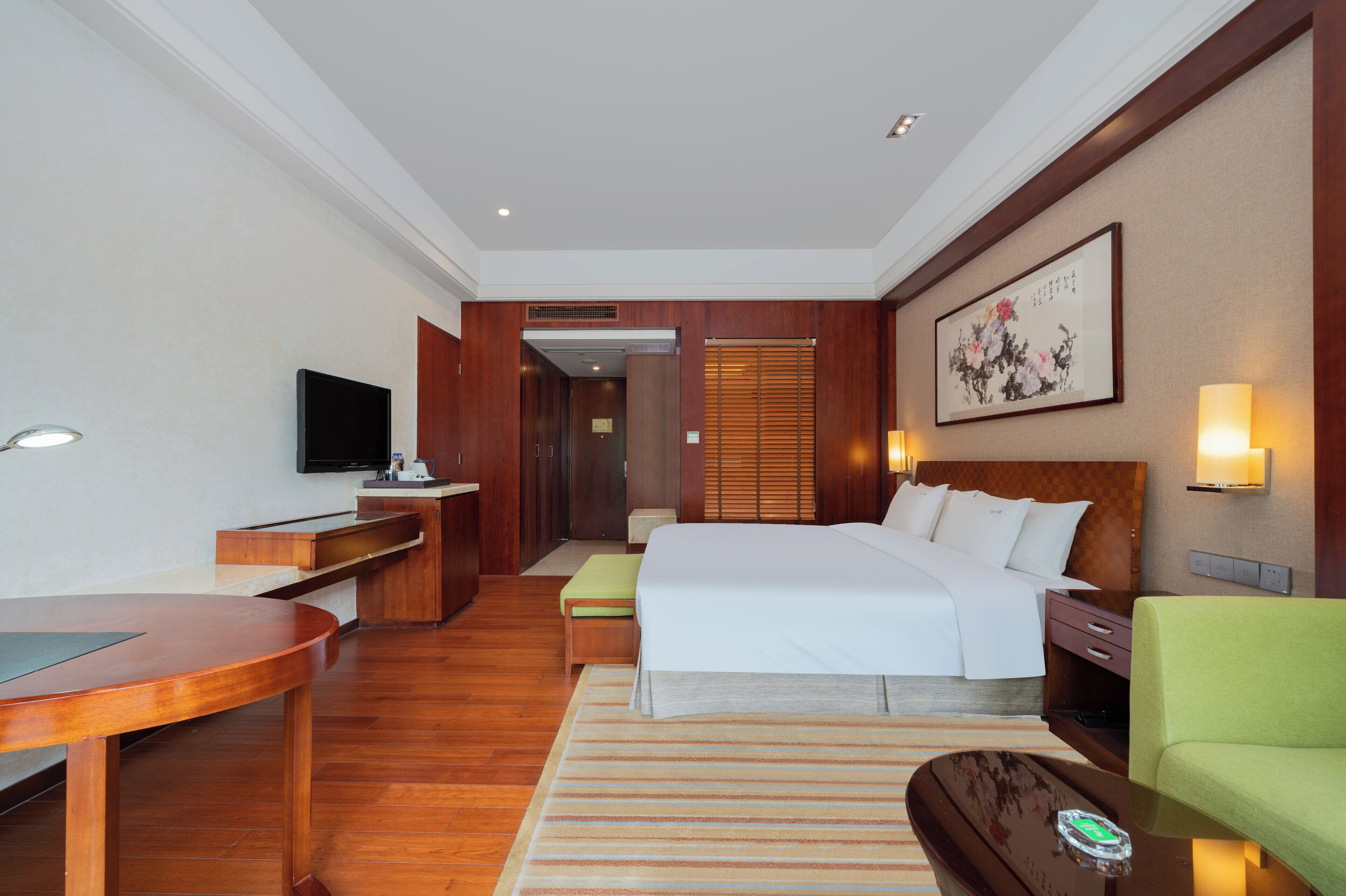 A hotel room with a bed, bedside table, TV, and a desk with a chair.
