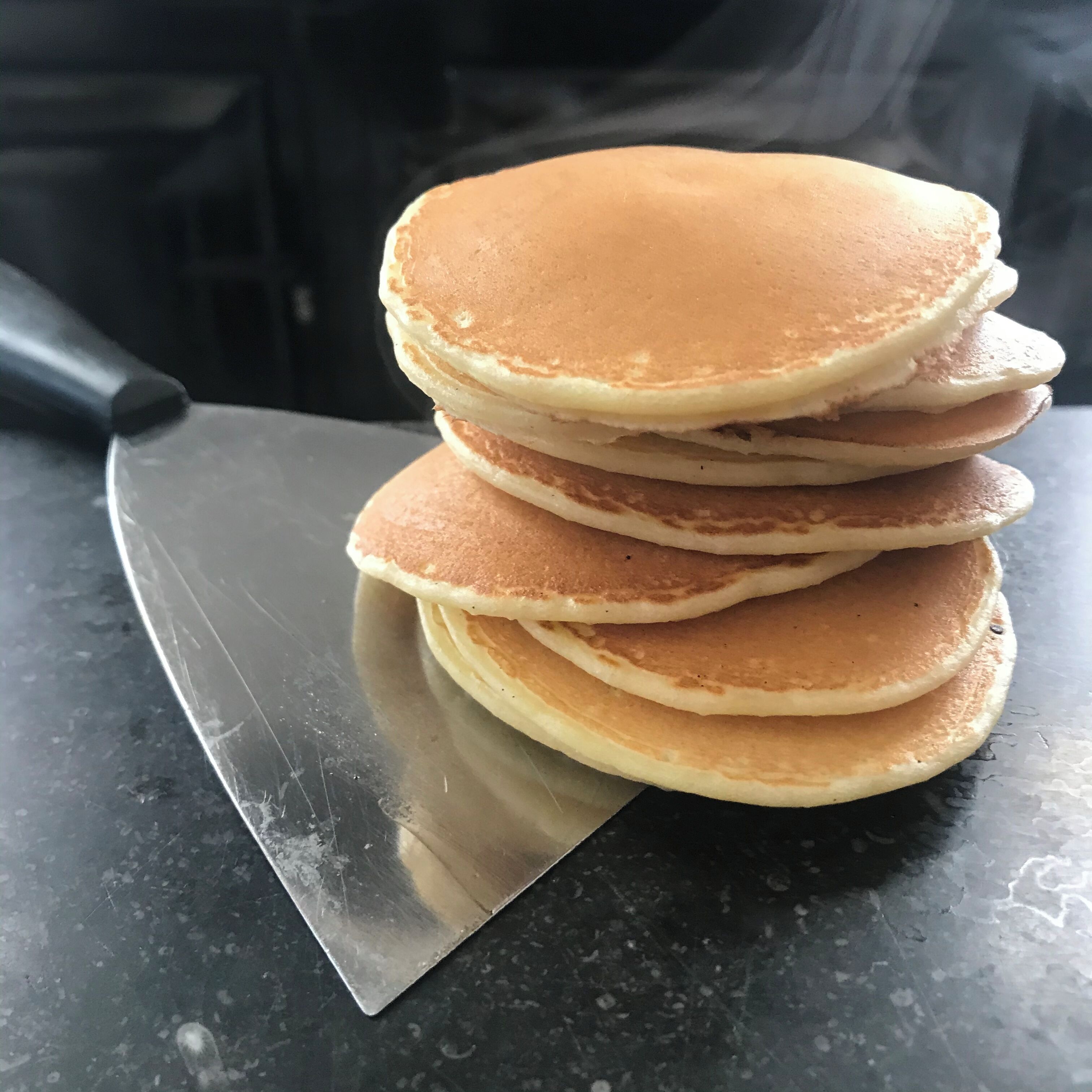 Een stapel pannenkoeken op een donker aanrecht, met een mes ernaast.