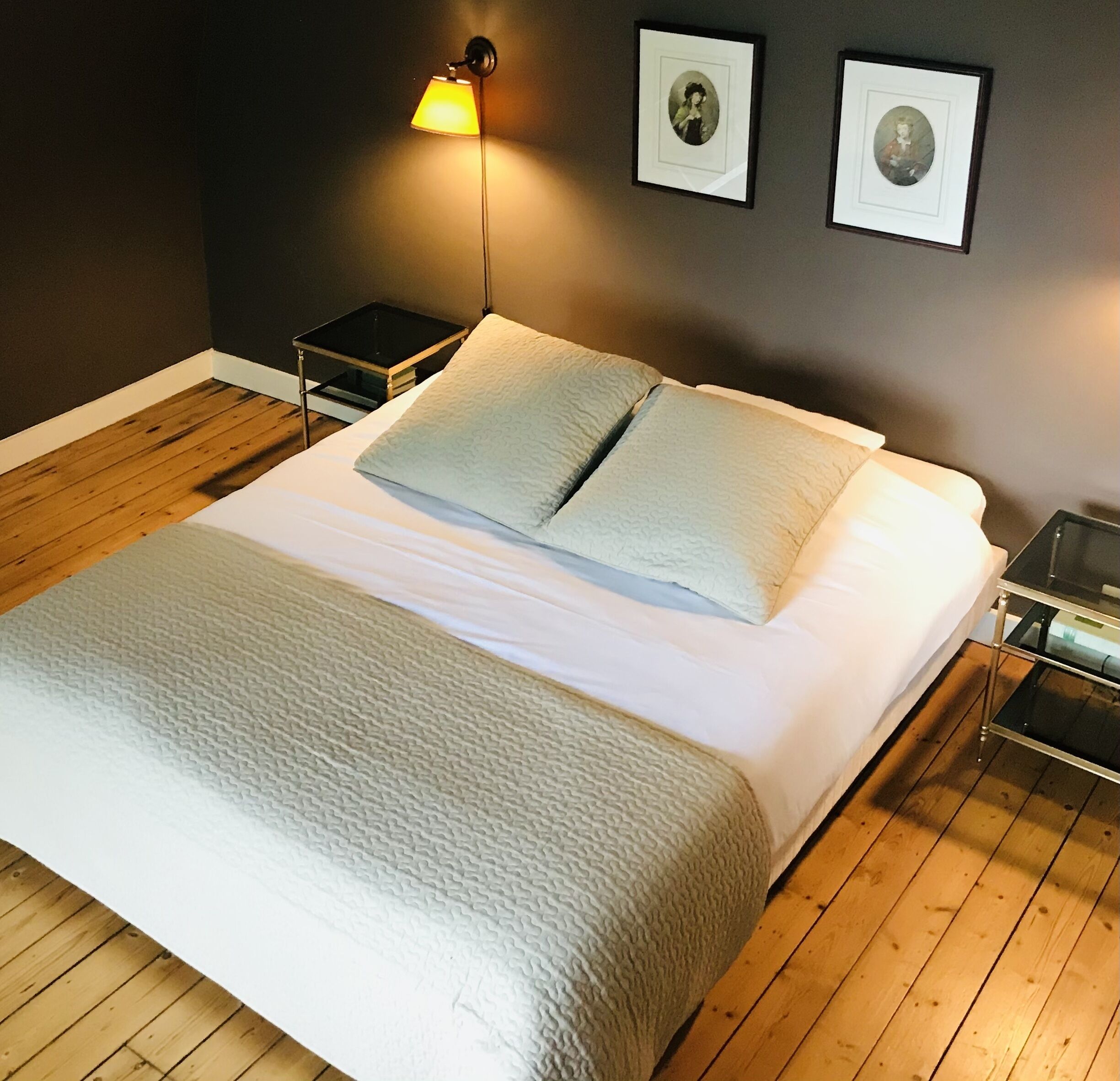 A neatly made bed with a white duvet and two pillows, a bedside table with a lamp, and two framed pictures on the wall.