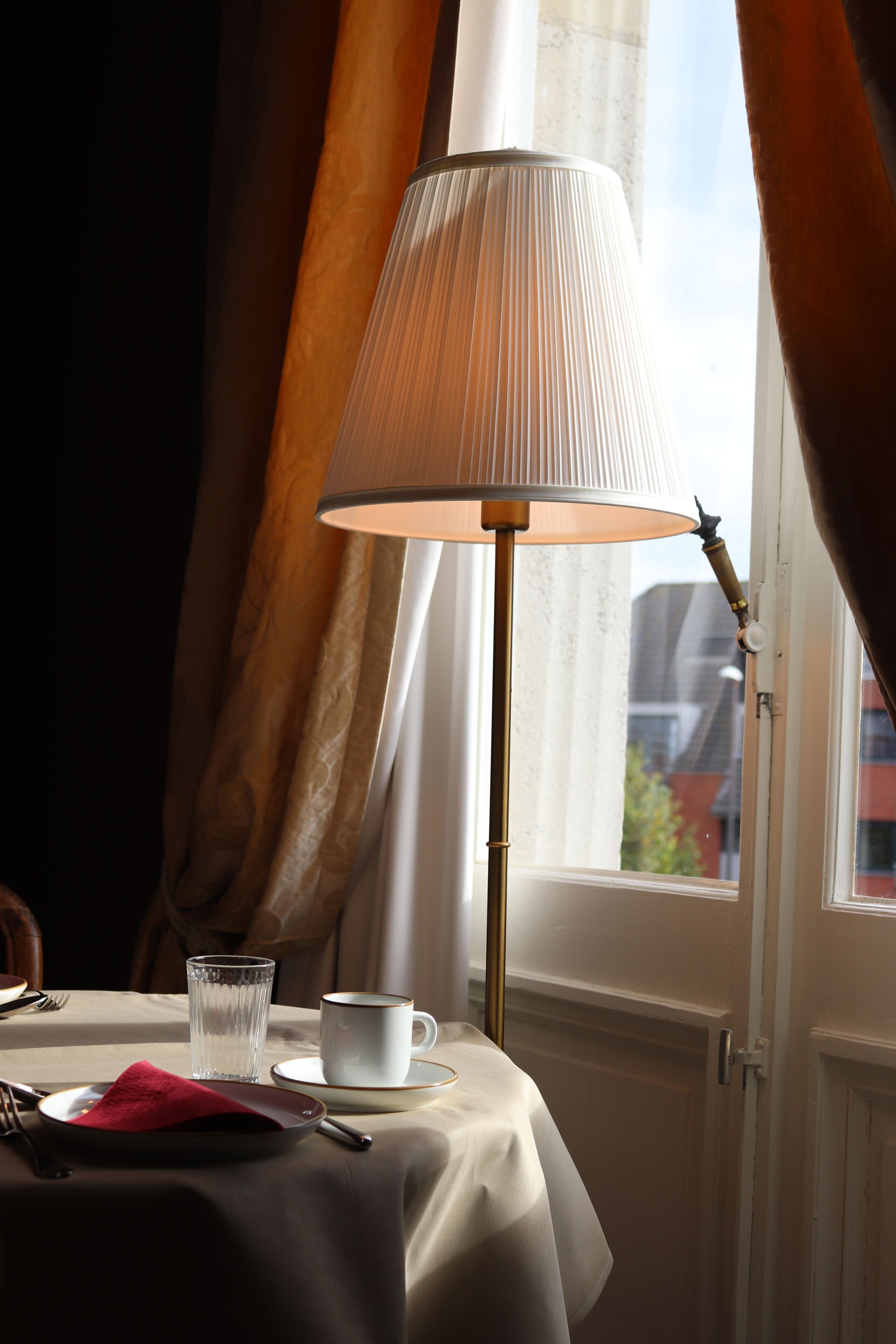 A table with a white tablecloth, a glass of water, a white cup, and a red napkin.