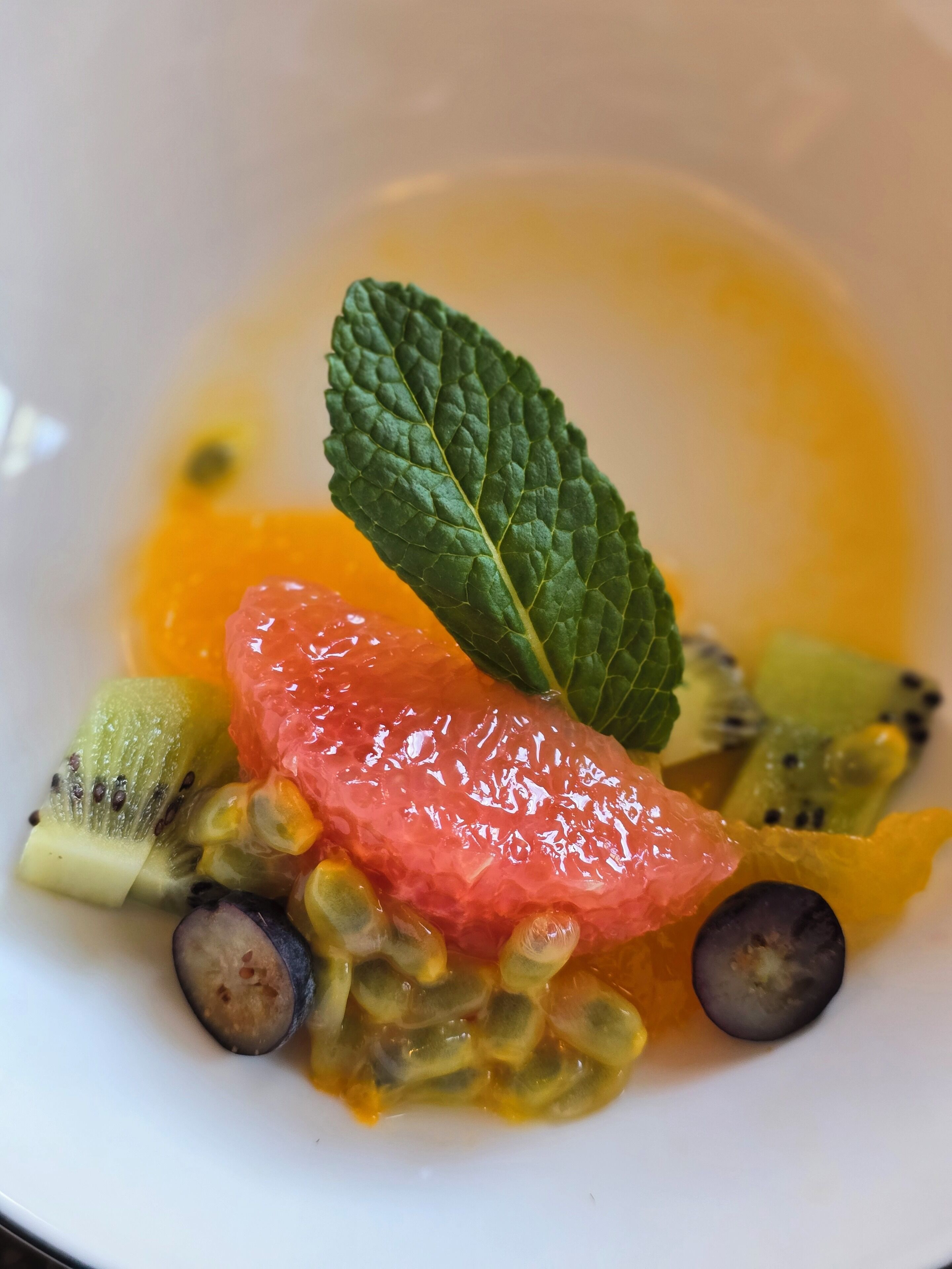 A plate with various fruits and a mint leaf.