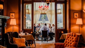 Un comedor con candelabro, mesas, sillas e imágenes enmarcadas en las paredes.
