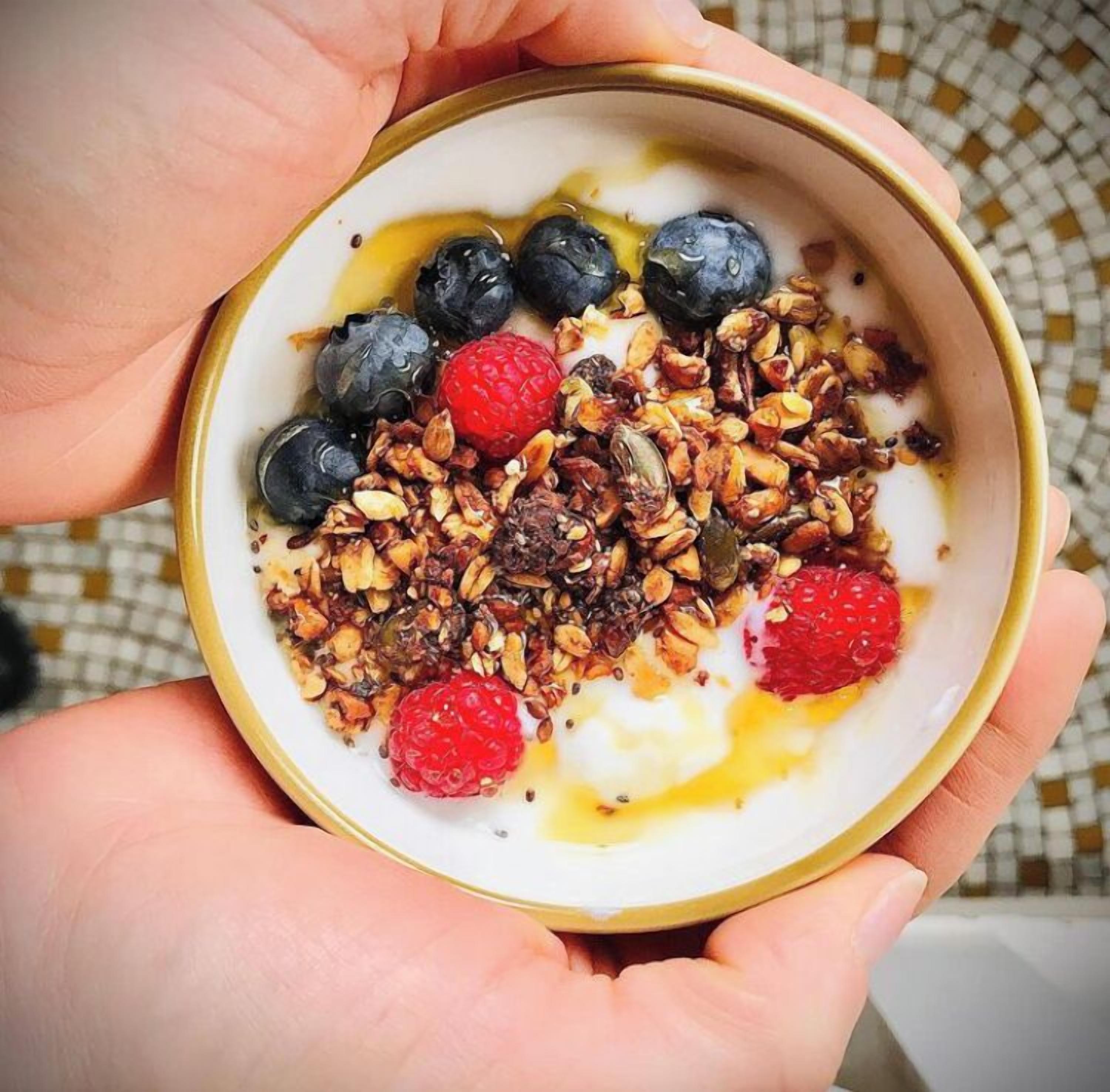 Un tazón de yogur cubierto de granola, arándanos, frambuesas y un chorrito de miel.