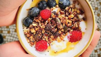Un tazón de yogur cubierto de granola, arándanos, frambuesas y un chorrito de miel.