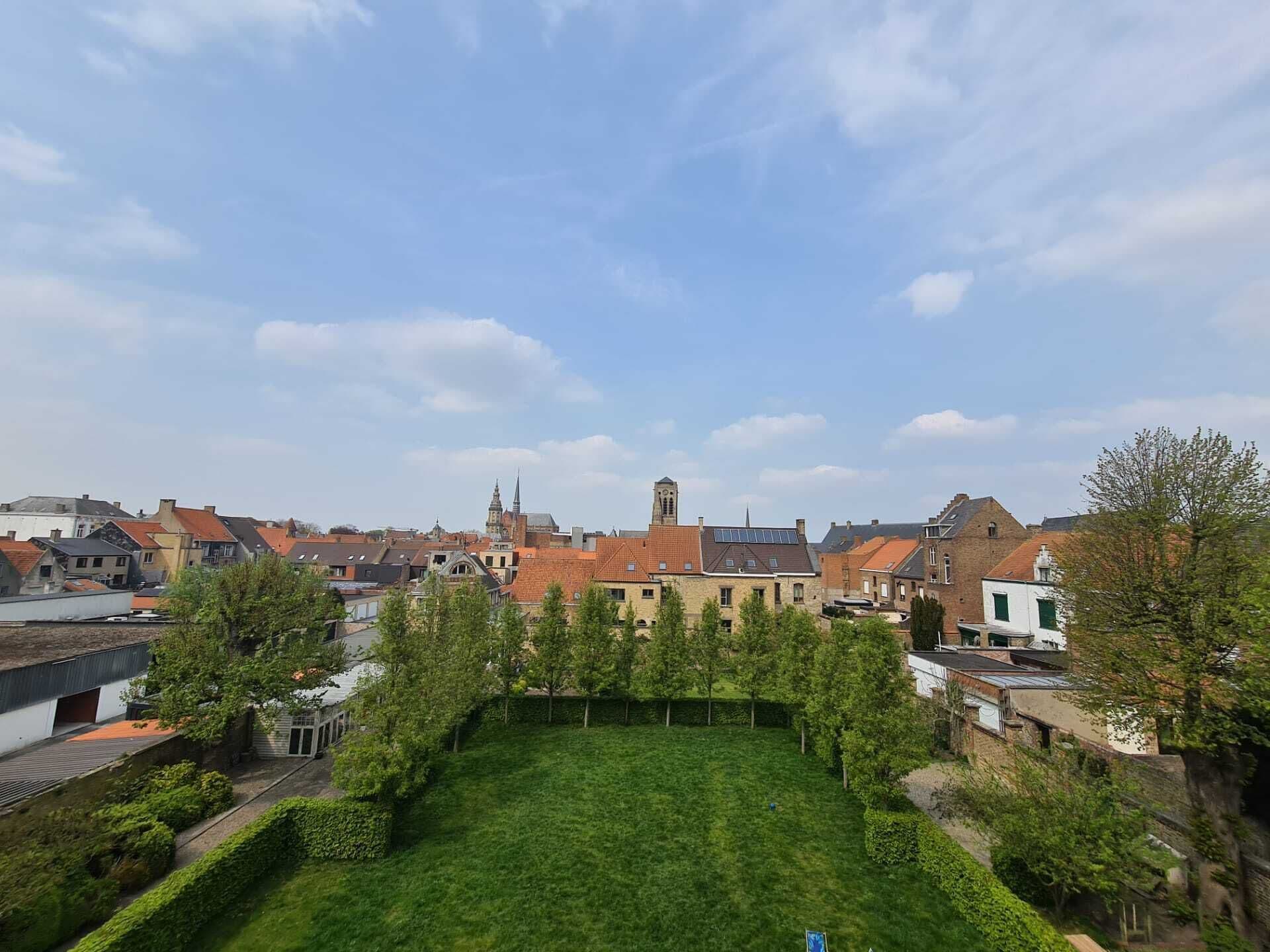 Vista de un pueblo con una destacada torre de iglesia, rodeado de edificios residenciales y un césped cuidado.