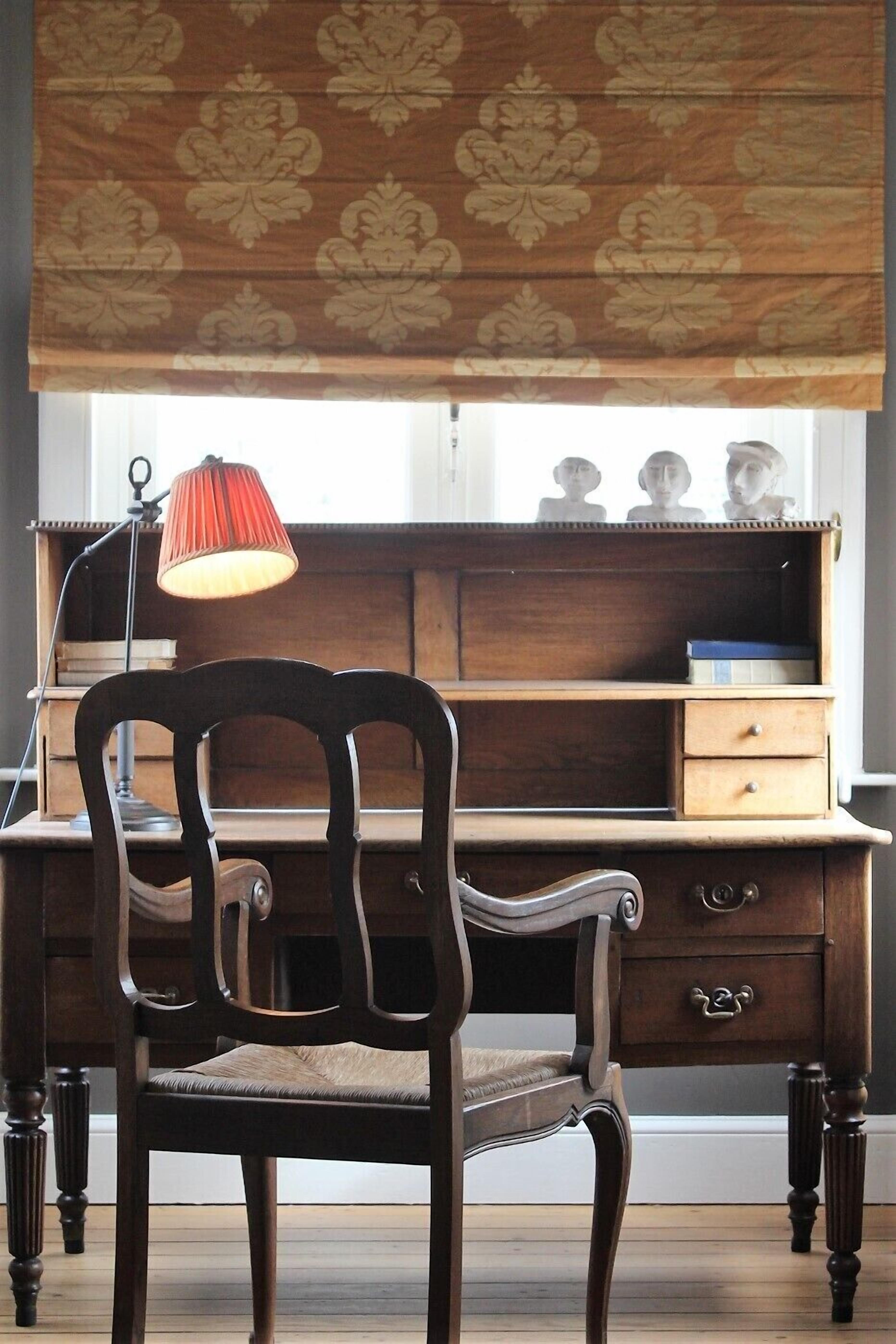 Un escritorio de madera con una lámpara, una silla y una ventana decorada.