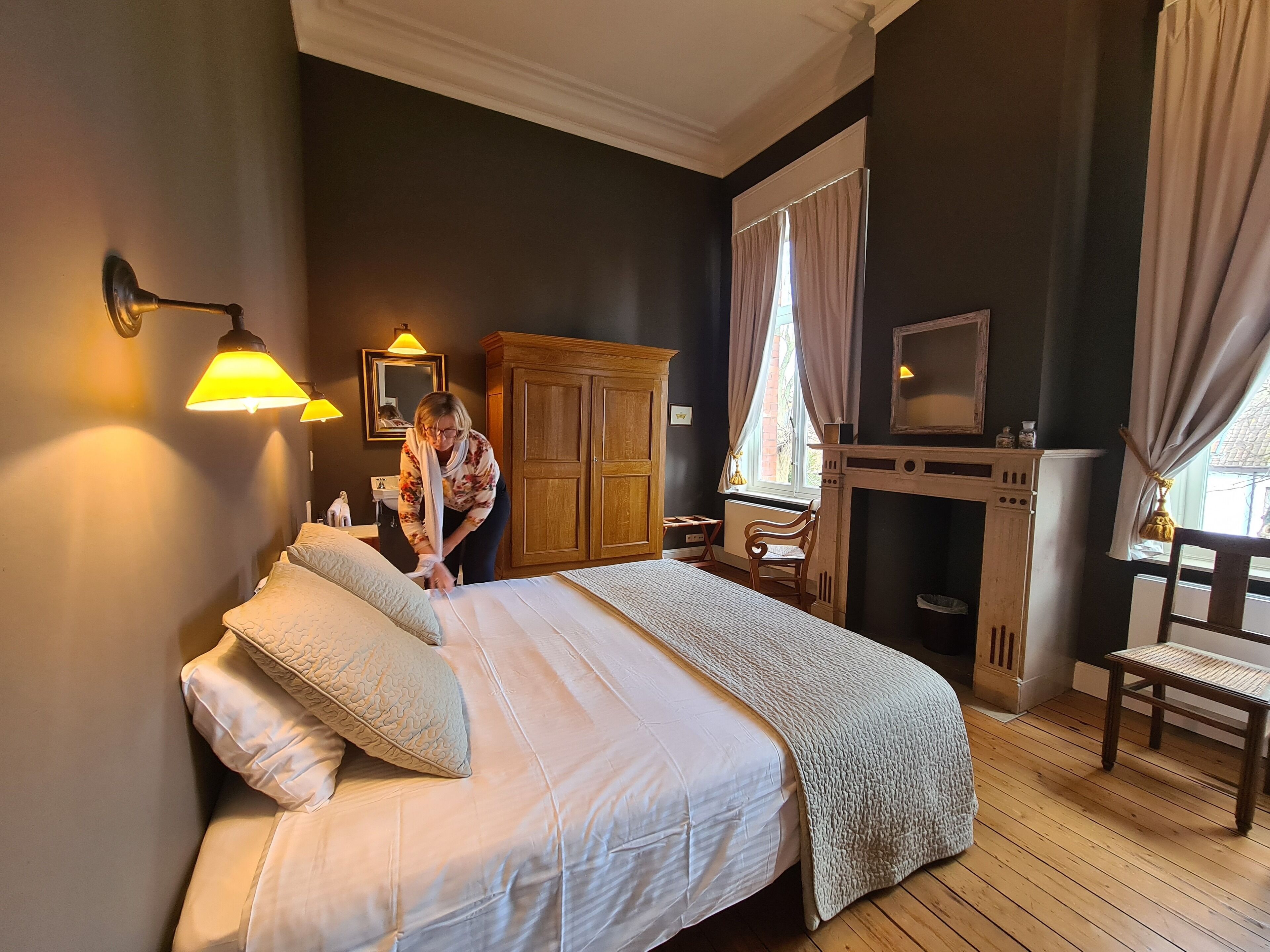A bedroom with a large bed, wooden wardrobe, and a fireplace.