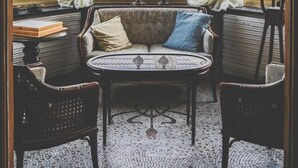 Un rincón acogedor con una mesa redonda, dos sillas, un sofá con cojines y una lámpara de araña.