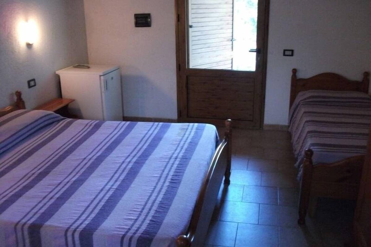 A bedroom with a large bed, a bedside table, a wardrobe, and a door leading to a balcony.