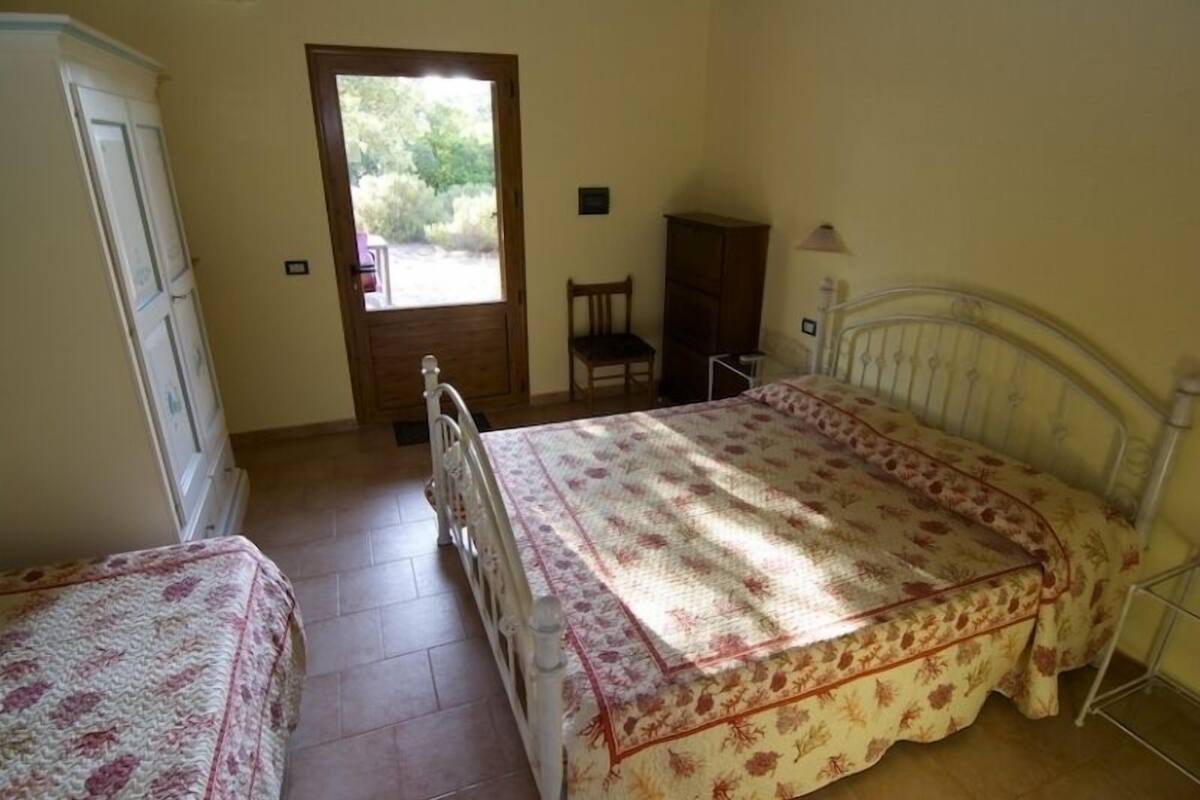 A bedroom with a bed, a chair, a wardrobe, and a door leading to an outdoor area.