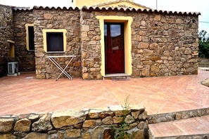 A stone building with a tiled patio, a wooden door, and a window with a wooden frame.