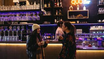 A bar with multiple shelves of bottles and glasses, a neon sign, and a counter with a menu.