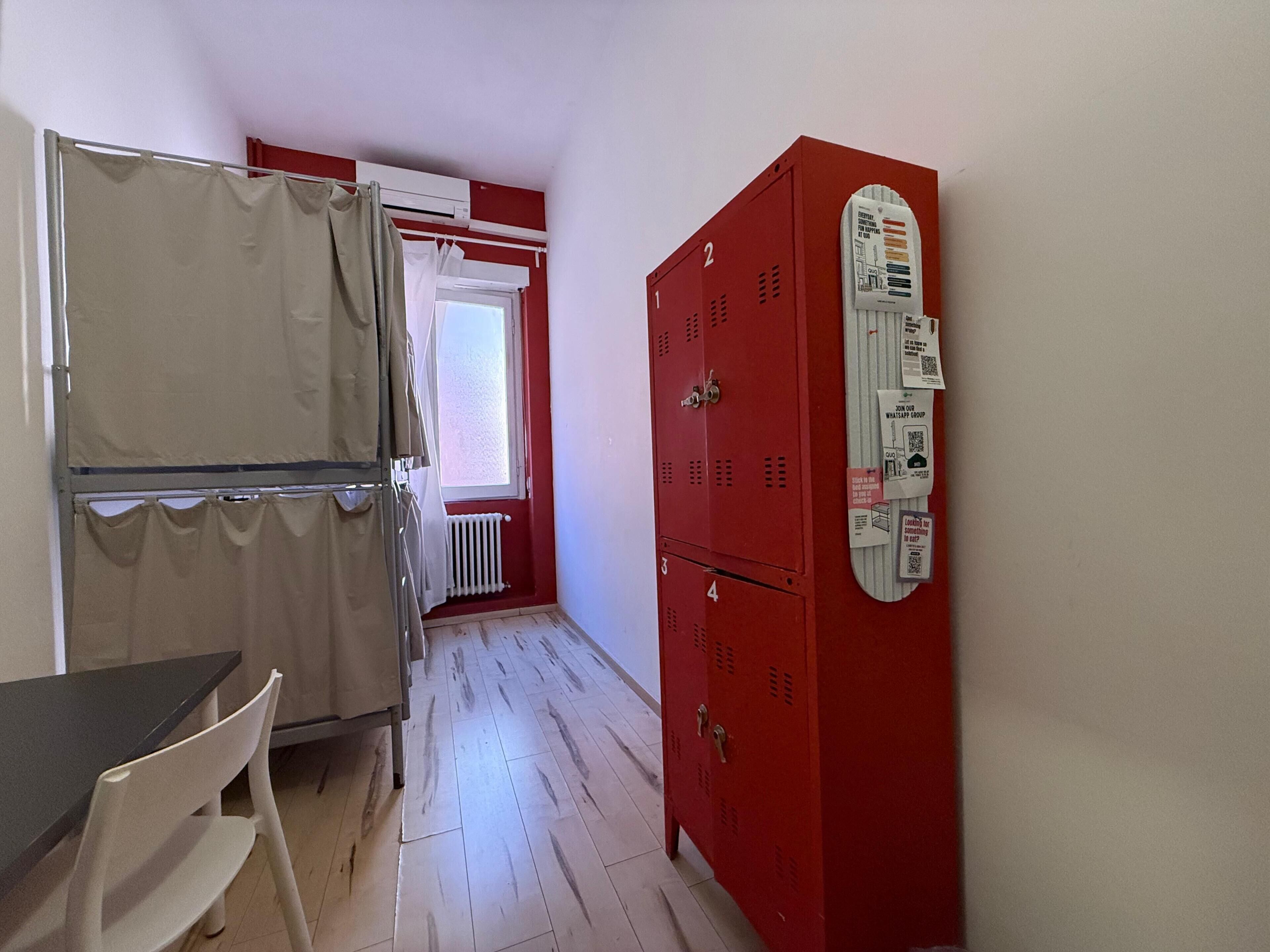 A room with a kitchenette, a table with a chair, and a red utility cabinet with a power outlet.