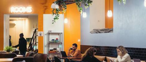 A cafe with tables and chairs, a sign reading "ROOMS", and hanging plants.