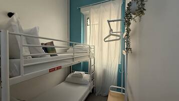 Habitación de dormitorio con literas, una ventana con cortinas, un equipo de aire acondicionado y una planta.