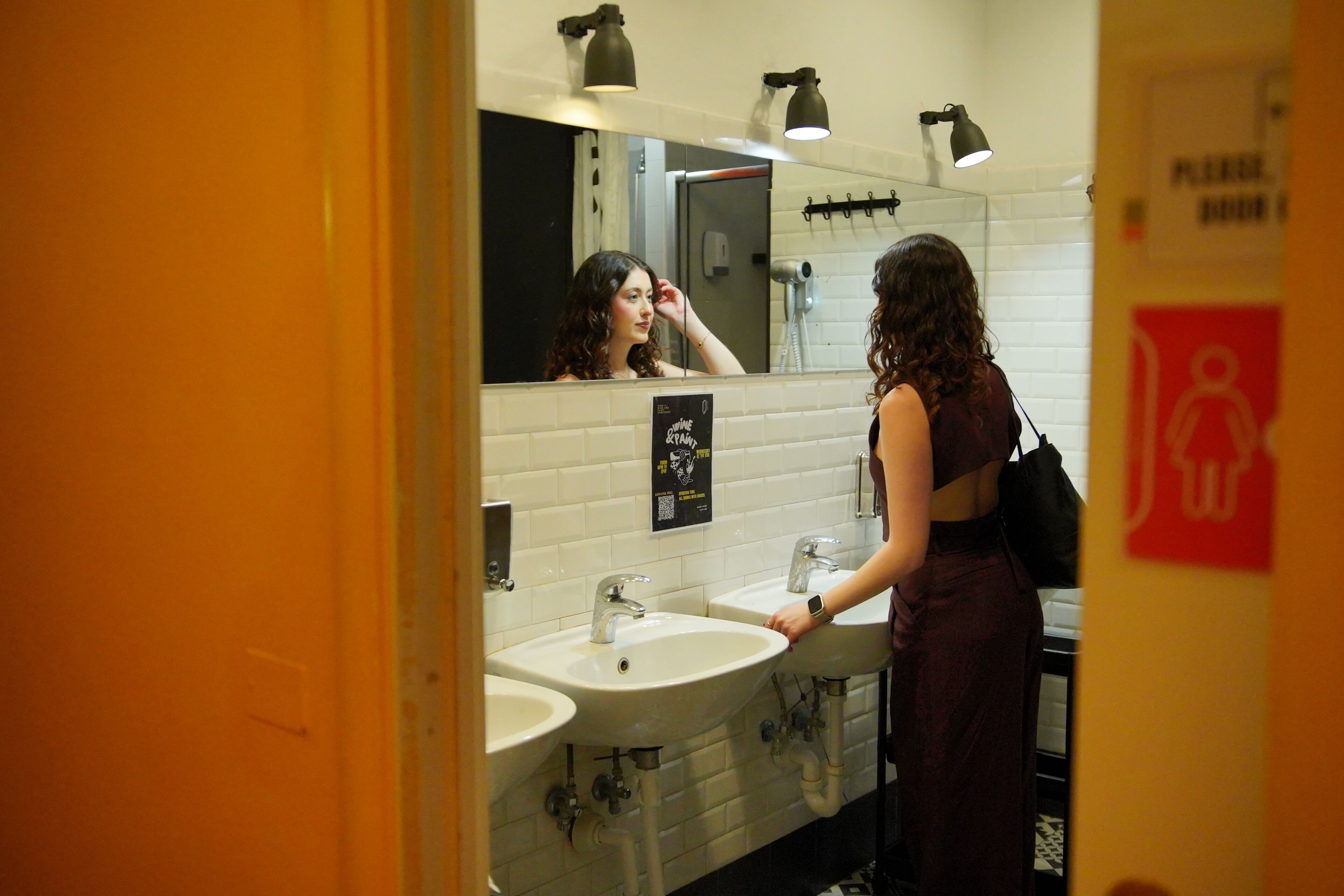 Baño público con tres lavamanos, un espejo y un letrero que indica zona de cambio para bebés.