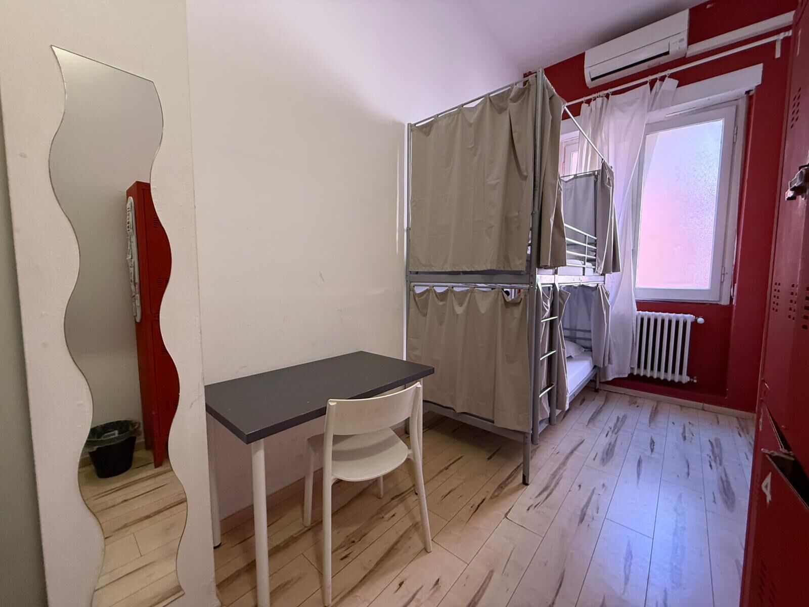 A small room with a bunk bed, a desk, a chair, and a radiator.