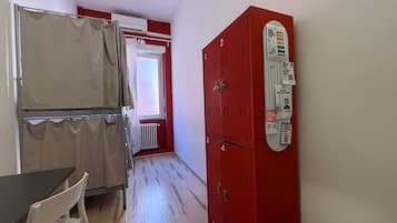 Ein Zimmer mit Tisch und Stühlen, einem Fenster mit Vorhängen und einem roten Funktionsschrank mit Bedienfeld.