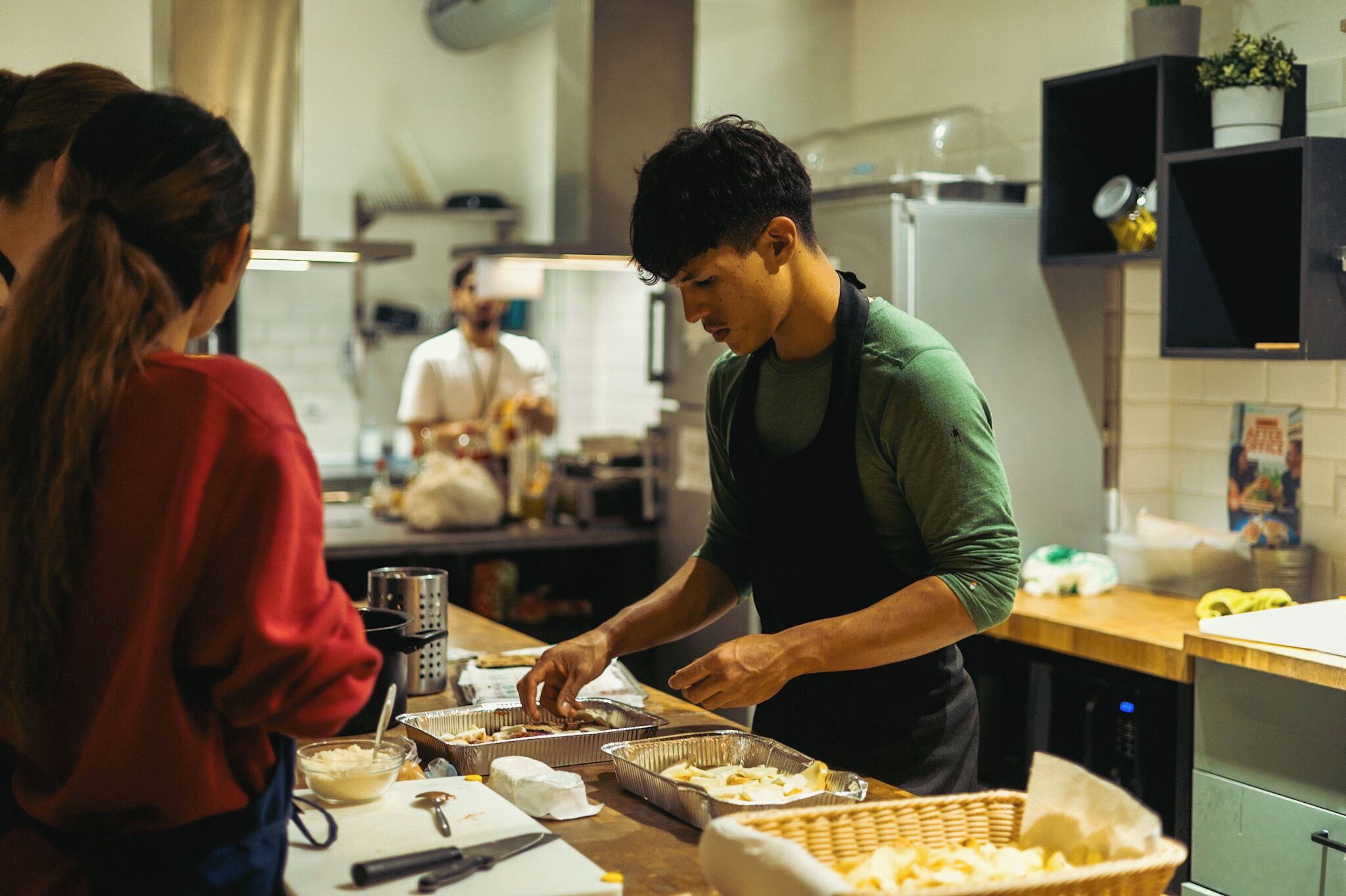 A person serving food in a kitchen with a counter and various food items.