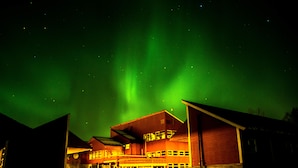 A building with a red exterior and multiple windows, under a night sky with green aurora borealis. - Tysfjord Turistsenter (Hamaroy)