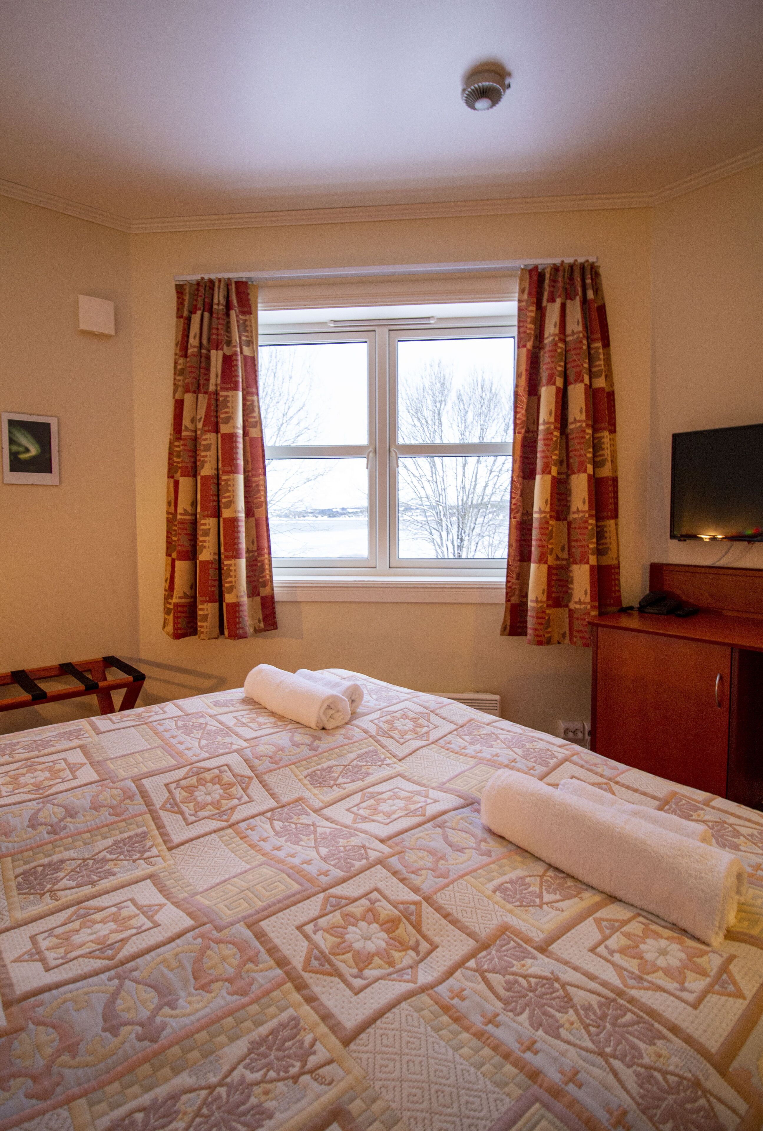 A hotel room with a large bed, a window with curtains, a television on a wooden cabinet, and a small table.