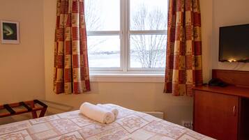 A hotel room with a large bed, a window with curtains, a television on a wooden cabinet, and a small table.