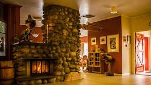 A stone fireplace with a fire, a wooden sign above it, and a tiled floor. - Tysfjord Turistsenter (Hamaroy)