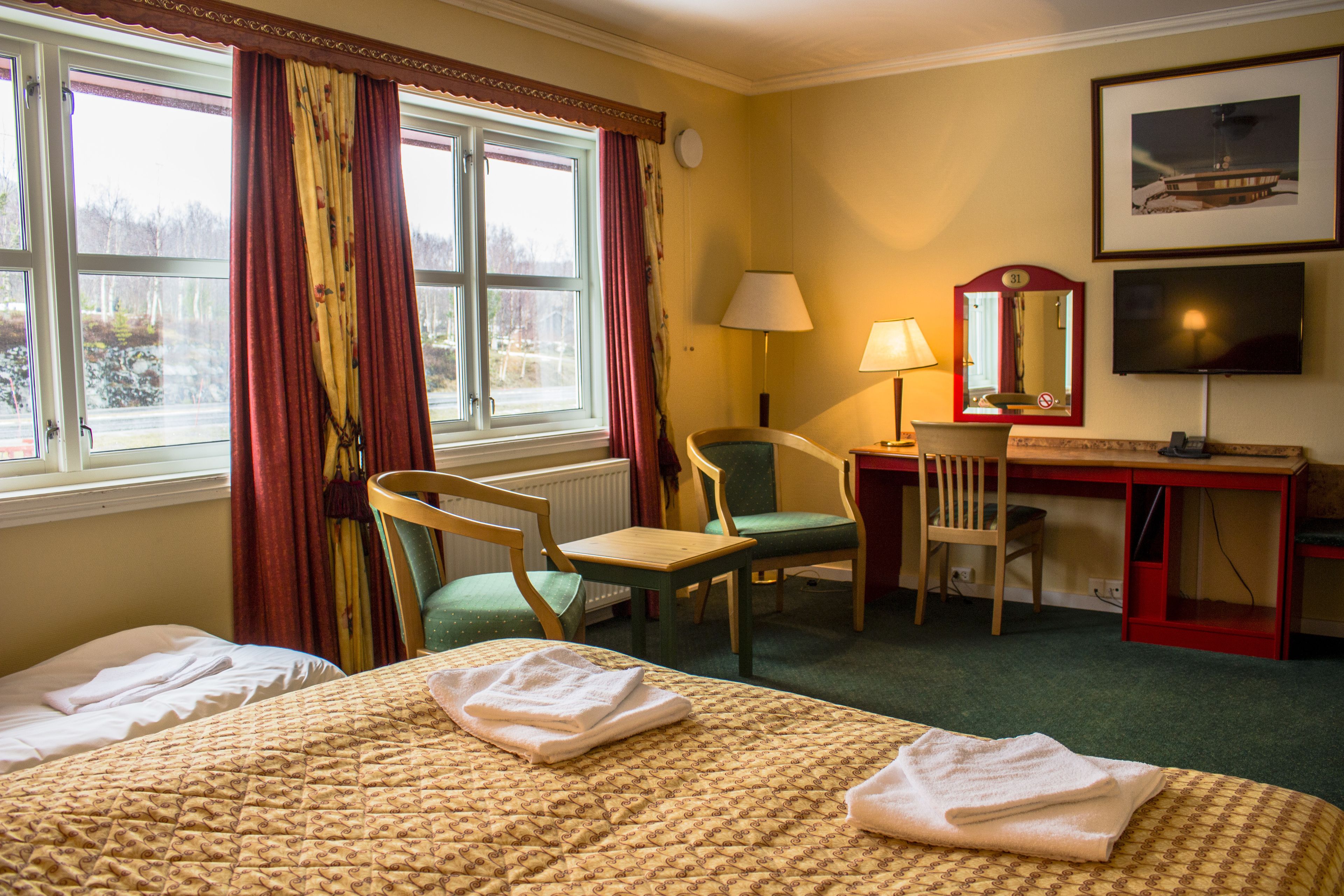A hotel room with two beds, a desk with a chair, a television, and a window with curtains.